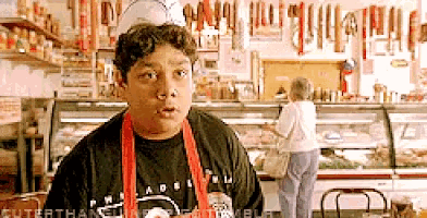 a man in a black shirt and red apron stands in a grocery store