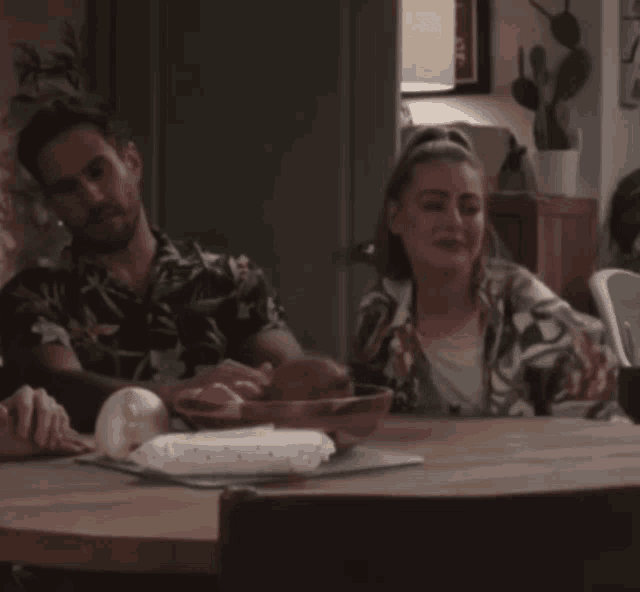 a man and woman sit at a table with a bowl of fruit on it