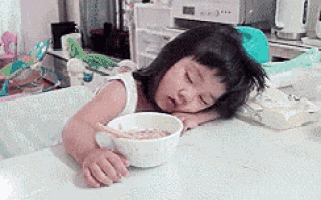a little girl is sleeping at a table with a bowl of cereal