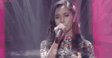 a woman is singing into a microphone while standing on a stage .