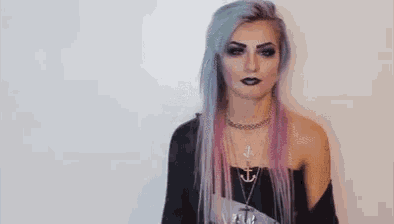 a woman with purple and blue hair is wearing a black top and a necklace .