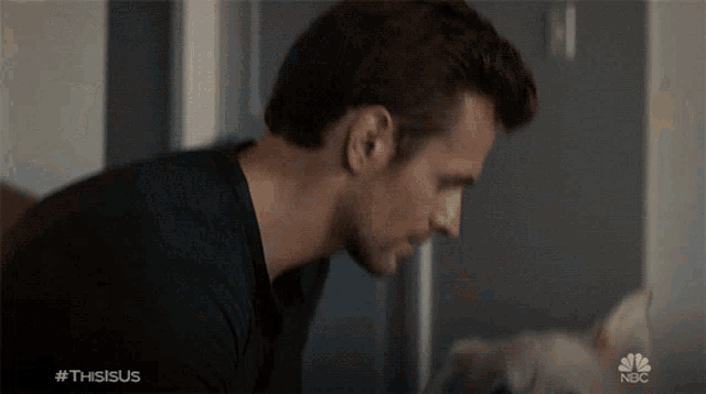 a man in a black shirt is looking at a cat with the hashtag #thisisus