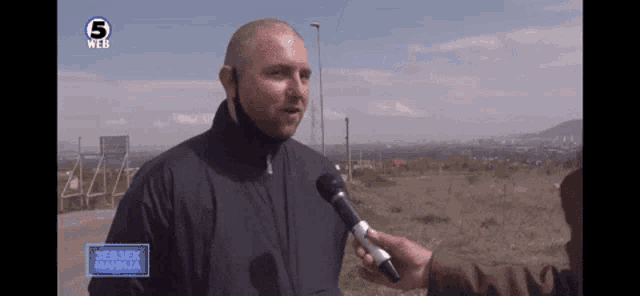 a man is being interviewed by a man with a microphone in front of a screen that says 5 web