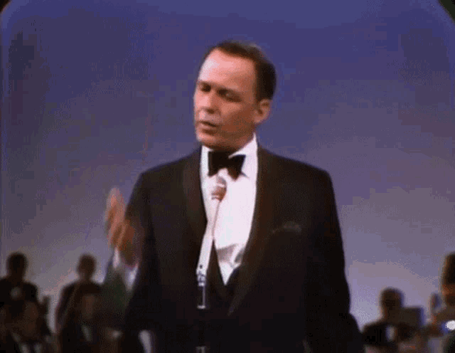 a man in a tuxedo and bow tie is singing into a microphone .