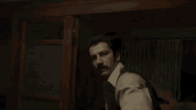 a man with a mustache is standing in a dark room in front of a door .