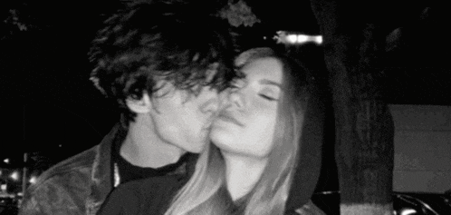 a boy and a girl are kissing in a black and white photo .