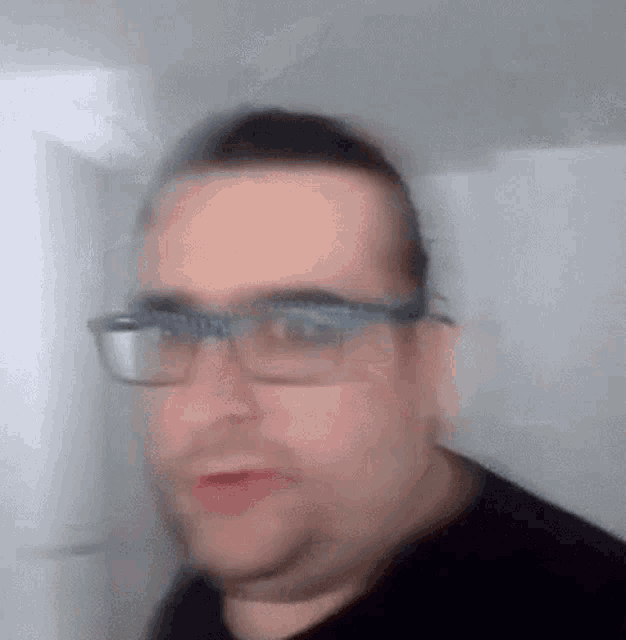 a blurry picture of a man wearing glasses and a black shirt .