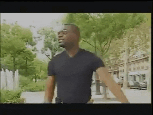 a man in a black shirt is walking down a street with his arms outstretched