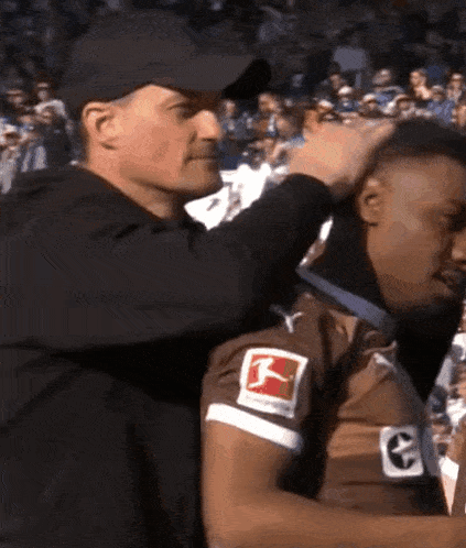 a man is putting a medal around a man 's neck who is wearing a jersey with the letter g on it