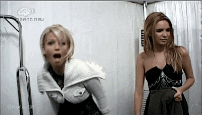 two women are standing next to each other in a room . one of the women is wearing a black dress .