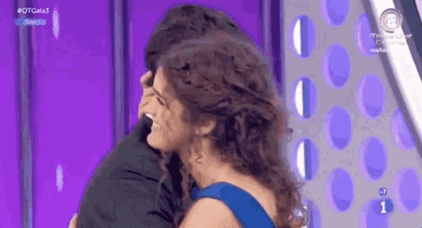 a woman in a blue dress is hugging a man in a black shirt on a purple background .