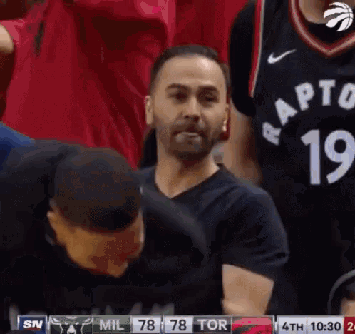 a man in a raptors jersey is sitting in the stands during a game .