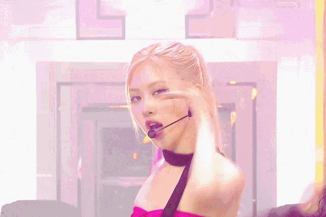 a woman wearing a pink top and a black choker holds her hair in a ponytail
