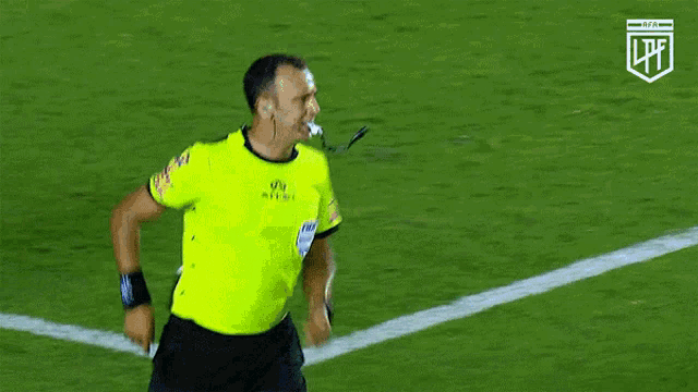 a referee wearing a yellow jersey that says lpfl stands on a soccer field