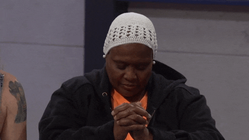 a woman wearing a white hat and a black jacket is praying with her hands folded