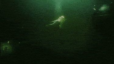a man is swimming underwater in a dark room in front of a green light .