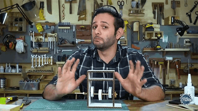 a man in a plaid shirt is making a funny face while holding a cardboard box in a workshop