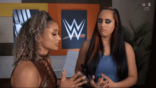 two women are talking in front of a wrestling logo