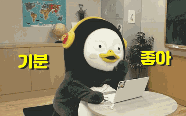 a stuffed penguin is sitting at a table with a laptop and headphones on