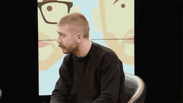 a man with a beard and mustache is sitting in a chair in front of a cartoon face .