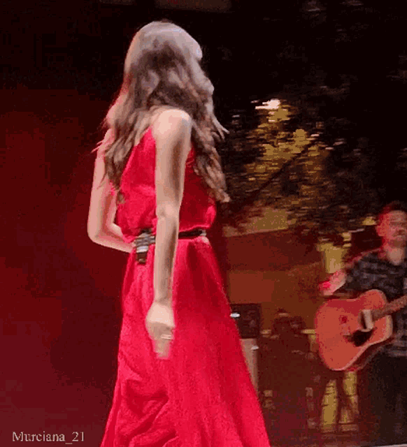 a woman in a red dress is dancing on a stage with a man playing a guitar behind her