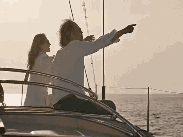 a man and a woman are sitting on a boat pointing at the ocean