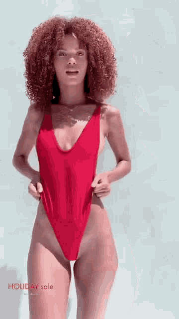 a woman in a red one piece swimsuit is standing in front of a blue wall .