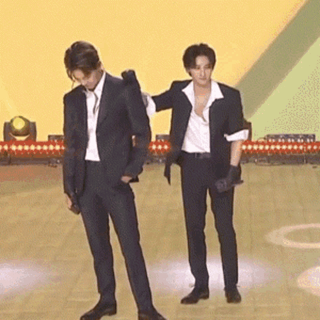 two men in suits standing next to each other on a stage
