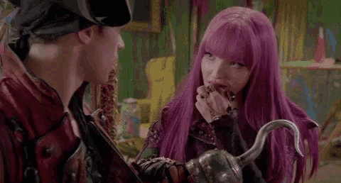 a man and a woman with purple hair are standing next to each other . the woman is holding a hook .