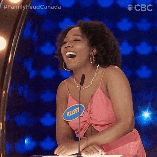 a woman in a pink dress is laughing in front of a microphone with a name tag that says kelsey .