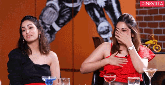 two women are sitting at a table with a pinkvilla logo in the background