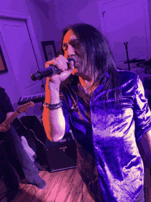 a man in a purple shirt is singing into a microphone in a room