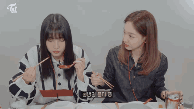 two girls are sitting at a table eating with chopsticks and the word twice is on the bottom left