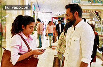 a man and a woman are standing next to each other in a mall and the woman is looking at her phone .
