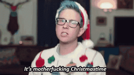 a man with blue hair and glasses is wearing a santa hat and a christmas sweater .