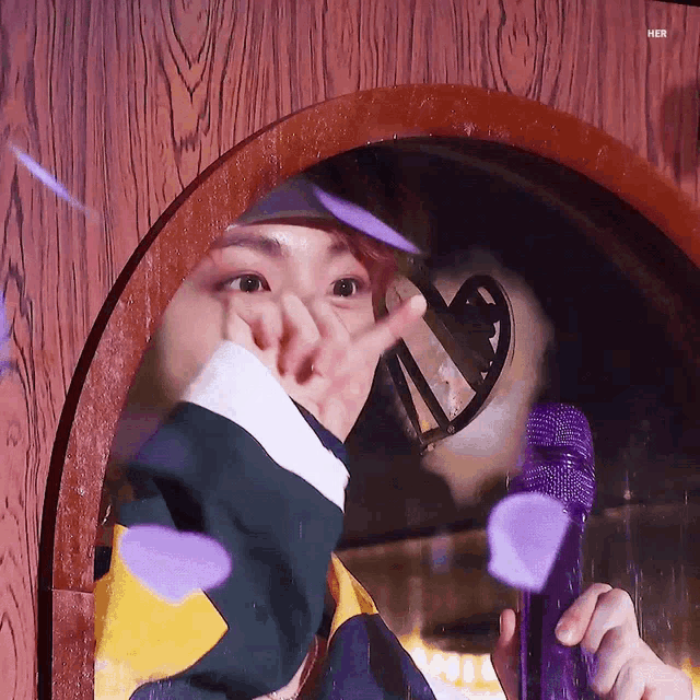 a person is holding a purple microphone and making a heart shape with their hand