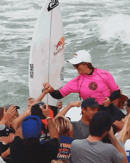 a surfer wearing a red bull shirt shakes hands with a group of people