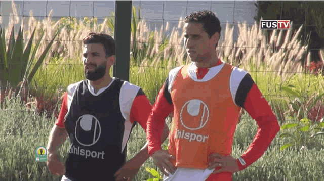 two soccer players wearing uhlsport vests are standing next to each other