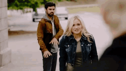 a man and a woman are walking down a sidewalk and the woman is wearing a denim jacket