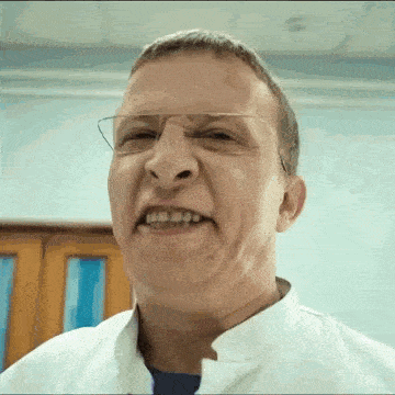 a close up of a man wearing glasses and a white coat making a funny face .