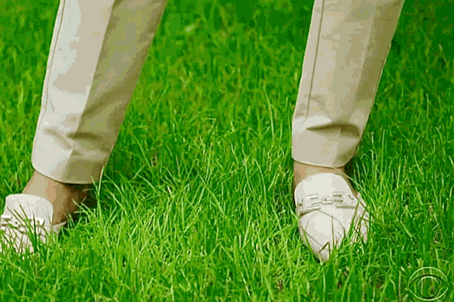 a person wearing white shoes is standing in the grass with a cbs logo in the background