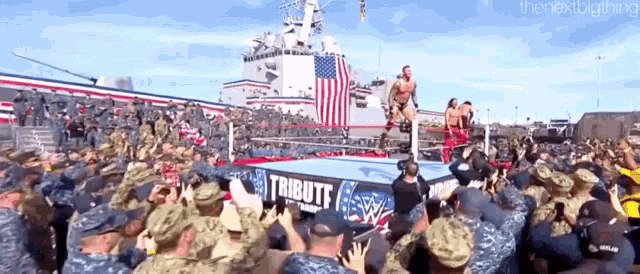 a crowd of soldiers are watching a wrestling match in front of a large american flag