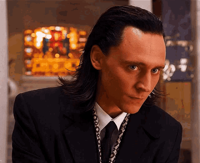 a man with long black hair wearing a black suit and tie
