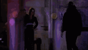 a man and a woman are standing in a dark room with a purple light behind them .