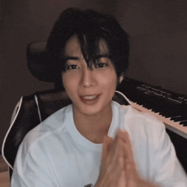 a young man in a white shirt is sitting in a chair in front of a keyboard