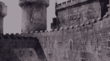 a black and white photo of a castle with a tower and a brick wall .