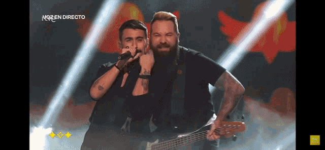 two men singing and playing a guitar on a stage in front of a sign that says no en directo