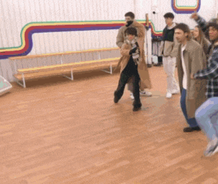 a group of people are dancing in a room with a rainbow on the wall behind them