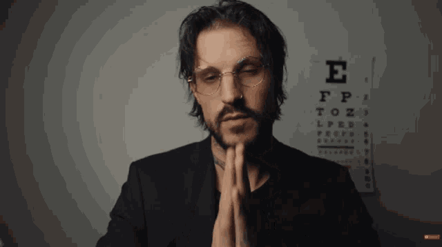 a man wearing glasses is praying in front of an eye chart that says e