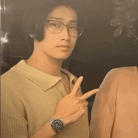 a man wearing glasses and a watch is giving the peace sign .